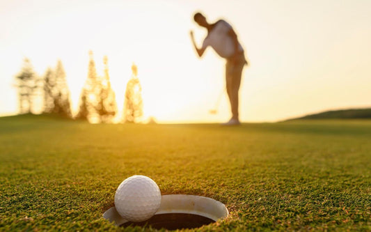 A golf ball falls into a hole on a green as a golfer completes his putt.