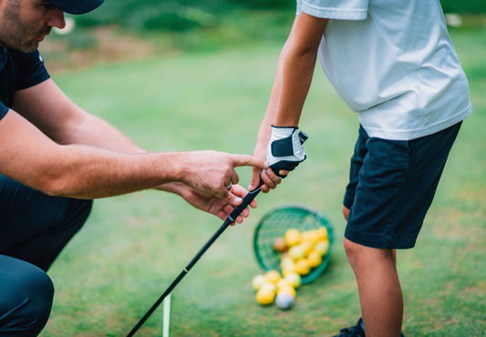 An instructor shows a child the interlocking golf grip, which involves intertwining the pinky finger of your trailing hand with the index finger of your lead hand.