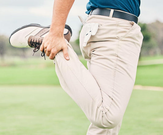 Golfer stretching by pulling one leg back while standing on a golf course.